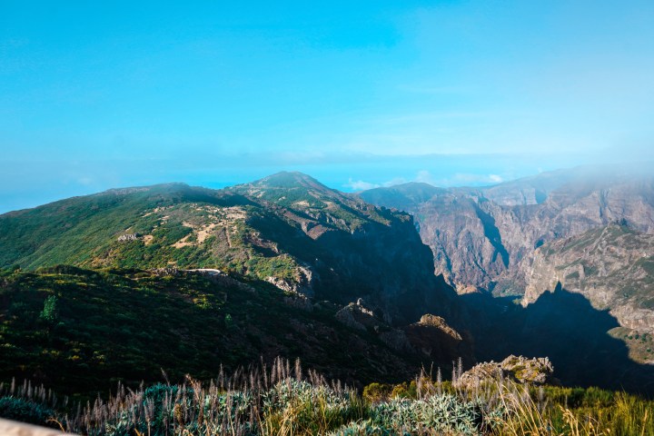 Mountain landscape with green hills, distant peaks, and a clear blue sky.