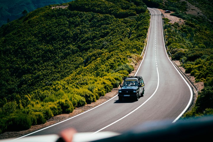 Car on winding road through lush green hills under blue sky.