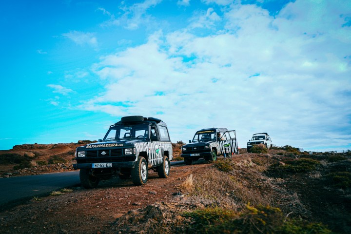 Three off-road vehicles on a scenic dirt road under a partly cloudy sky.