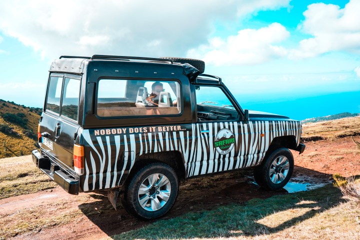 Safari jeep with zebra stripes parked on a hill with ocean view.