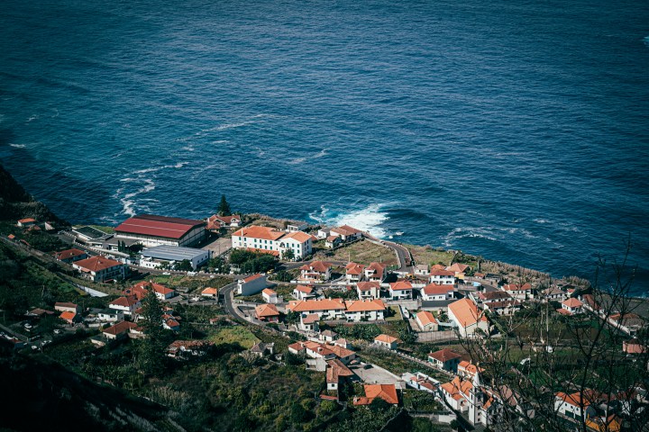 Coastal village with red roofs near ocean waves and rugged cliffs, under clear sky.