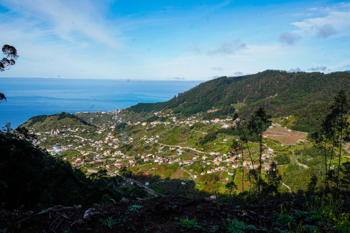 Coastal village with green hills and ocean view under a blue sky.