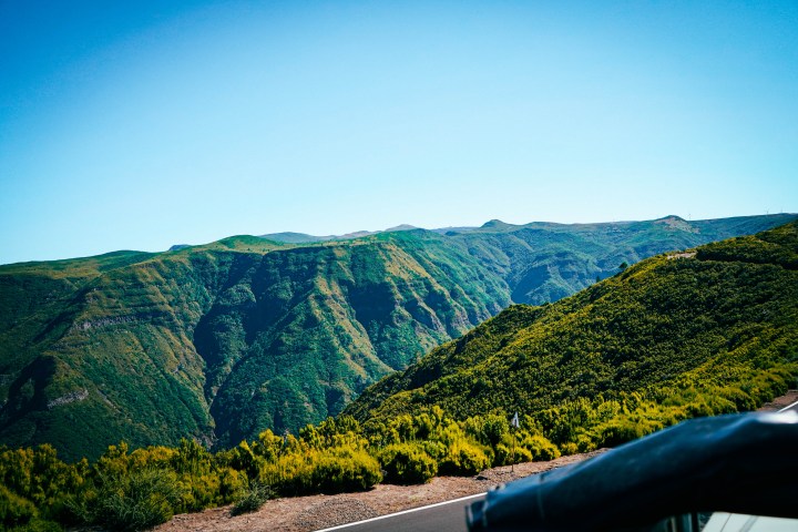 Lush green mountains under a clear blue sky with a road in the foreground.