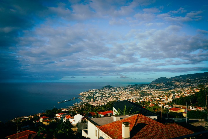 A coastal cityscape with red-roofed buildings under a partly cloudy sky.