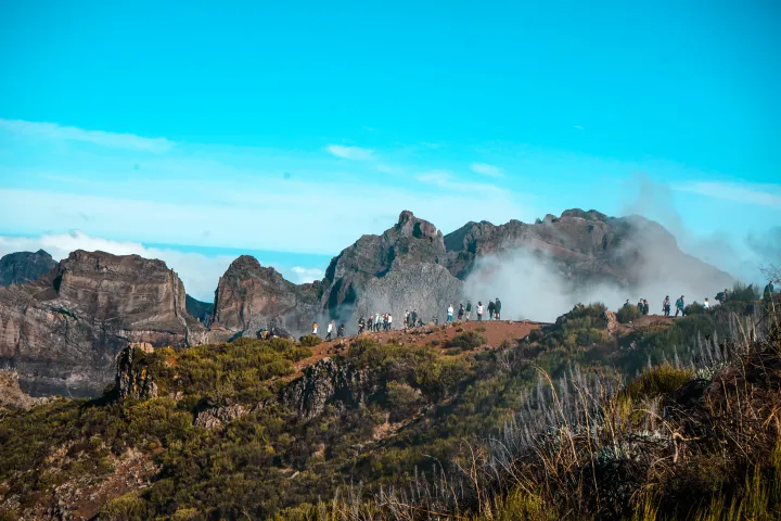 Mountains with people walking on a foggy ridge under a clear blue sky.
