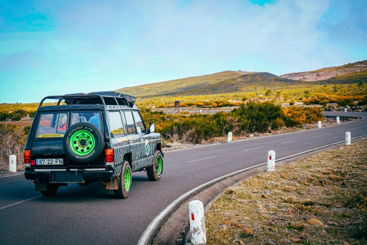 Truck with green wheels on winding road in scenic countryside.