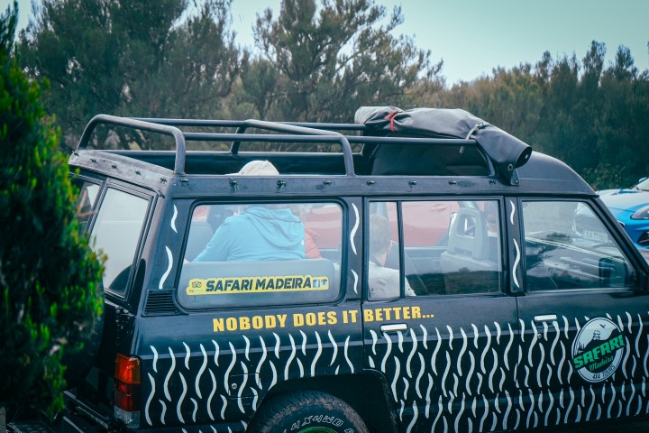 Black safari jeep with roof rack, parked near trees.