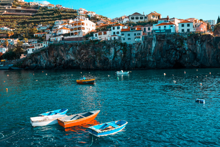 Colorful boats floating on clear water with cliffside houses and terraced hills in the background.