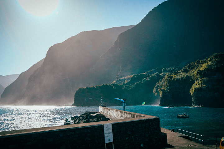 Sunlit coastal cliffs with a pier and a small boat on the water.