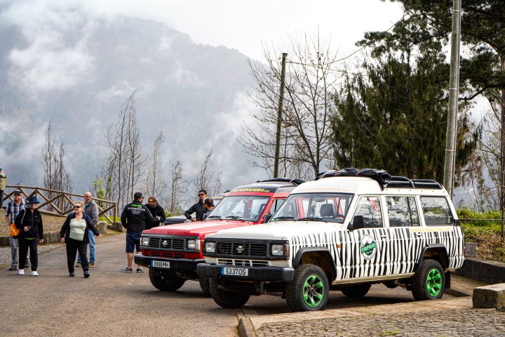 Two safari vehicles parked with people nearby in a mountainous area with mist and trees.